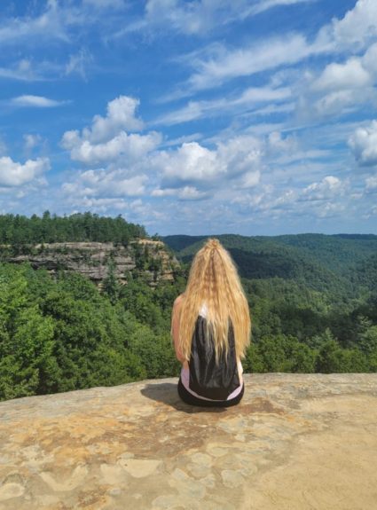 girl sitting on edge of rock looking out at landscape