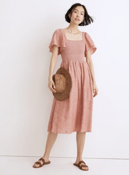 girl standing wearing peach colored dress and holding hat